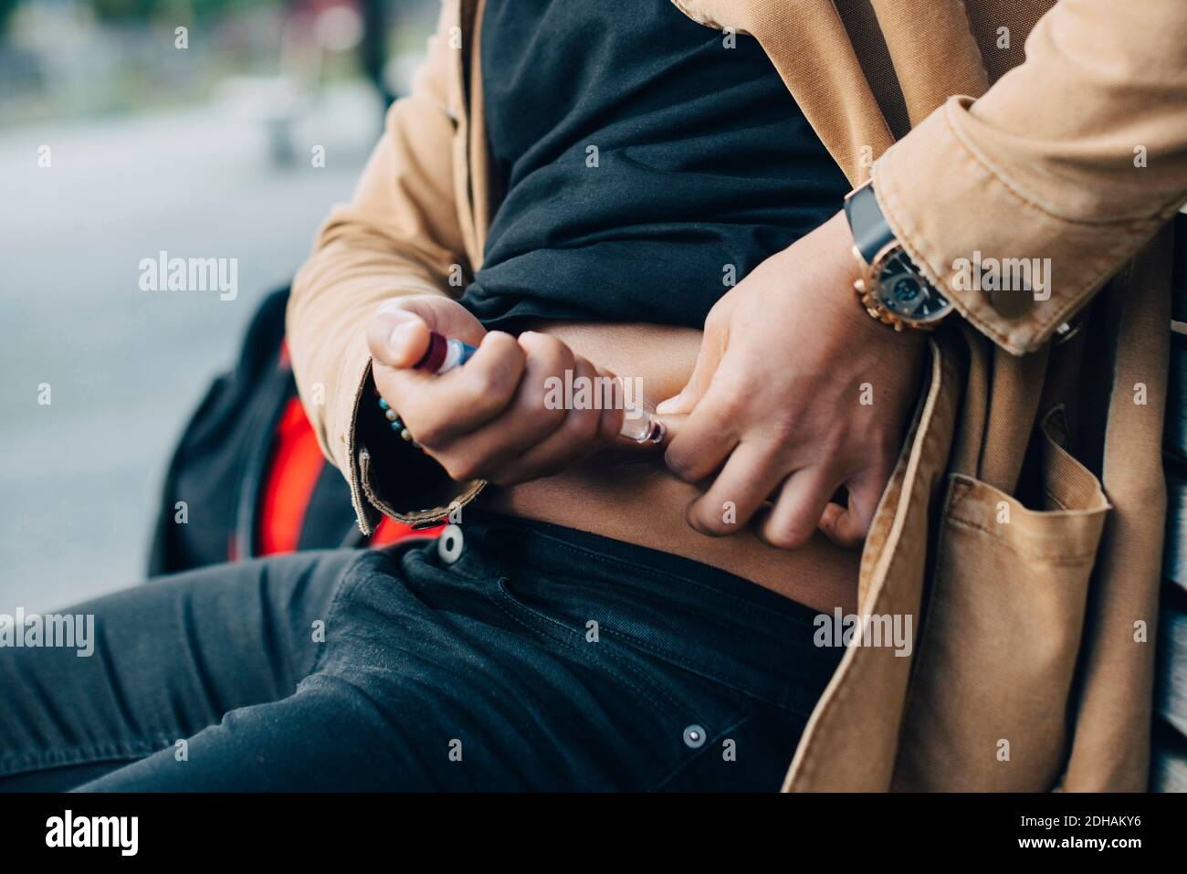 Midsection of man injecting insulin while sitting on bench Stock Photo