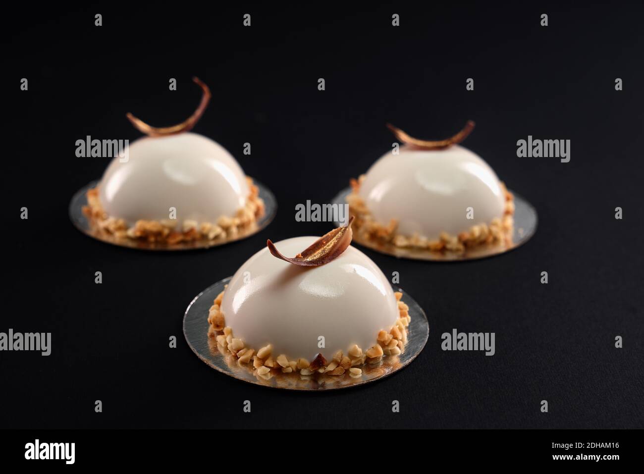 White half sphere cakes decorated with nuts and chocolate feather isolated on black background. Dessert with smooth surface, mousse and mirror glaze. Stock Photo