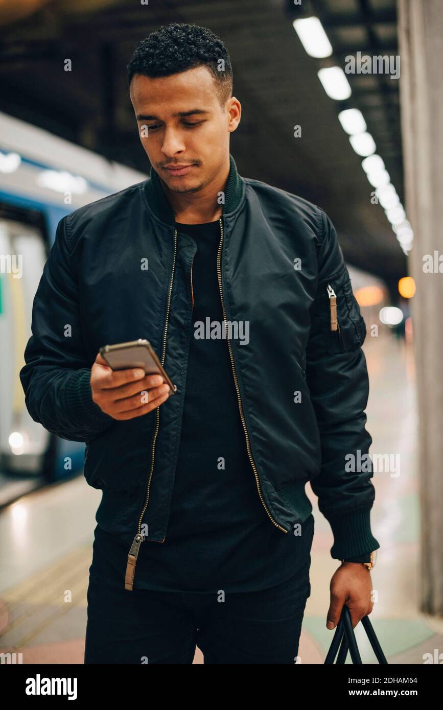 Man using mobile phone while standing by train at subway station Stock Photo