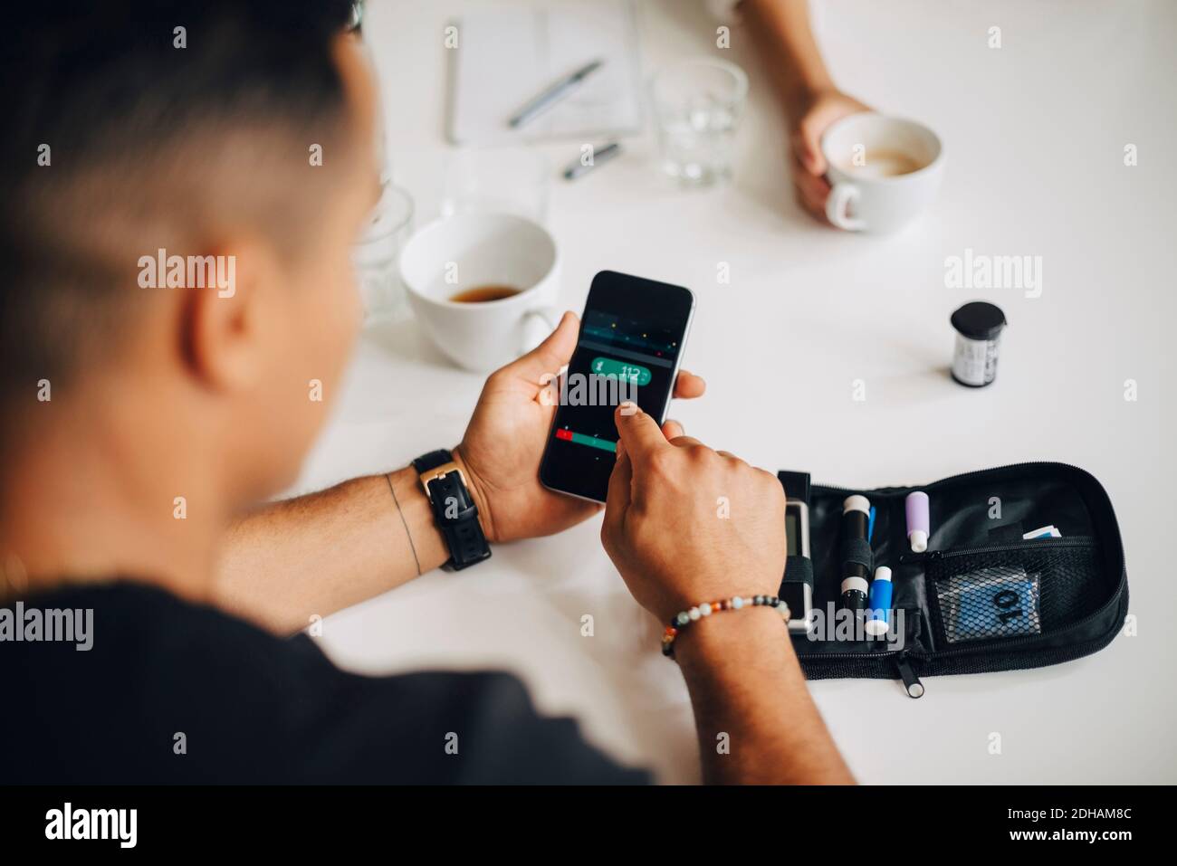 Businessman using mobile phone while doing blood sugar test at table during coffee break Stock Photo