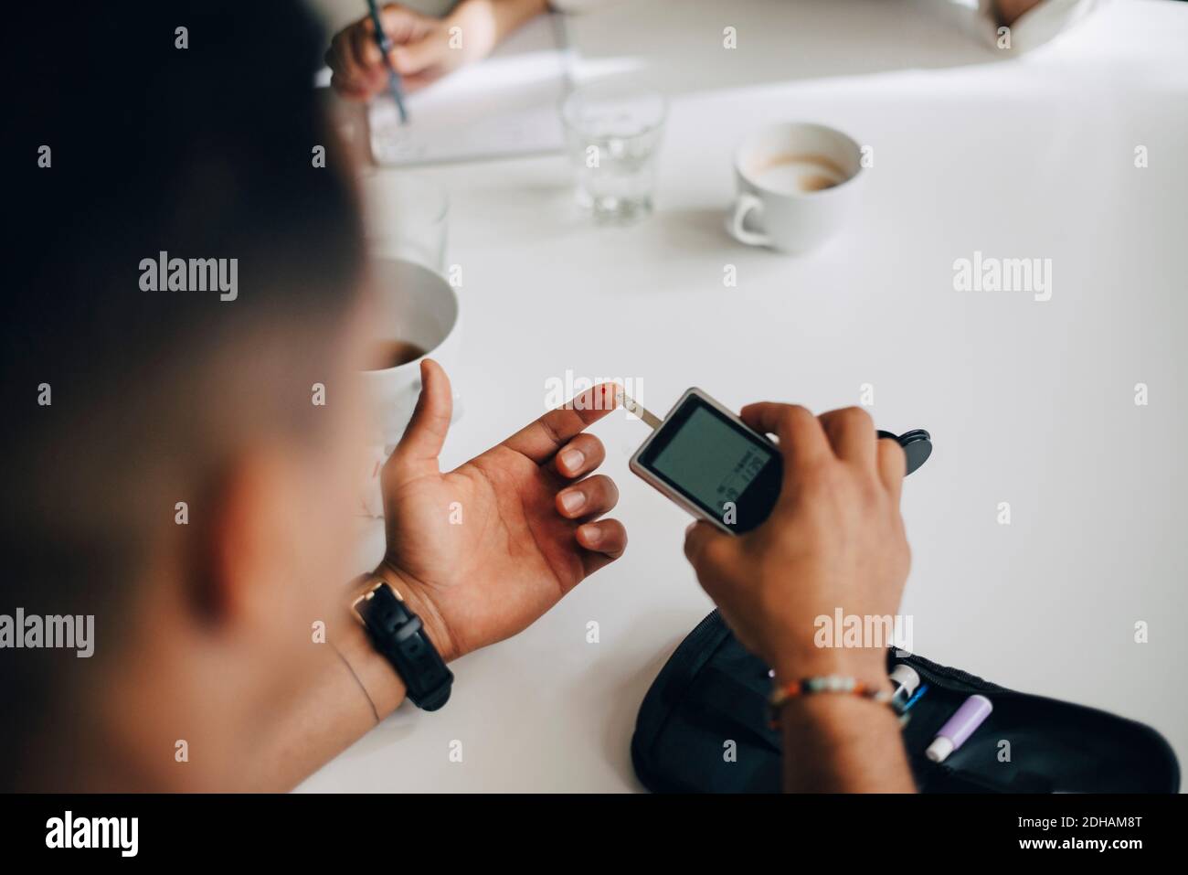 Businessman checking blood sugar level with glaucometer at table Stock Photo