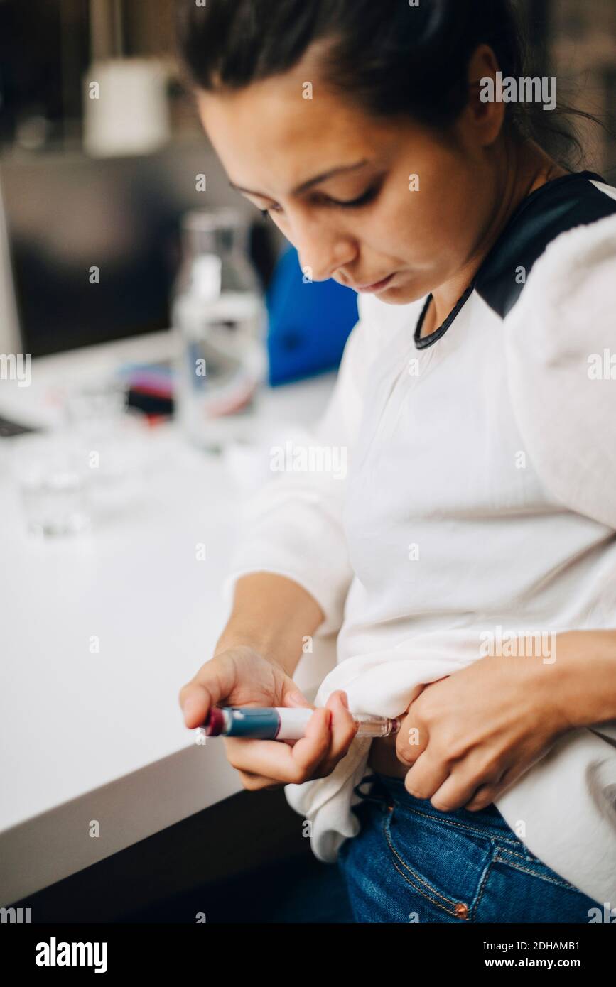 Businesswoman injecting insulin while sitting at table Stock Photo