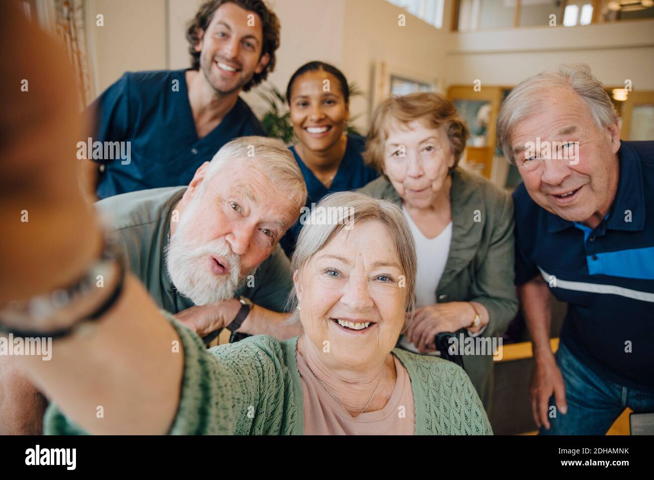 Retired elderly woman taking selfie with friends and caregivers at retirement home Stock Photo