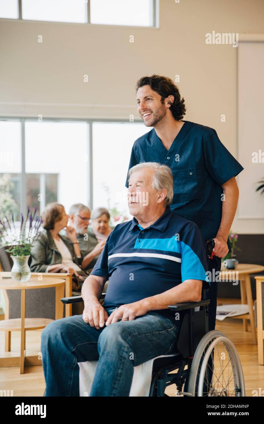 Smiling male nurse pushing disabled senior man on wheelchair at retirement home Stock Photo