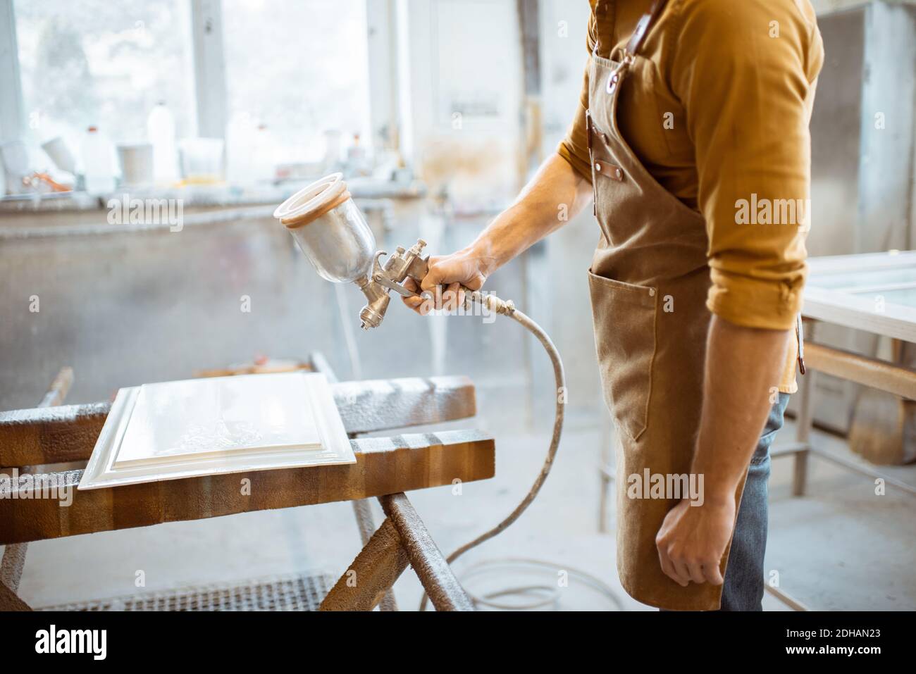 Worker painting wooden product with a spray gun at the painting shop of