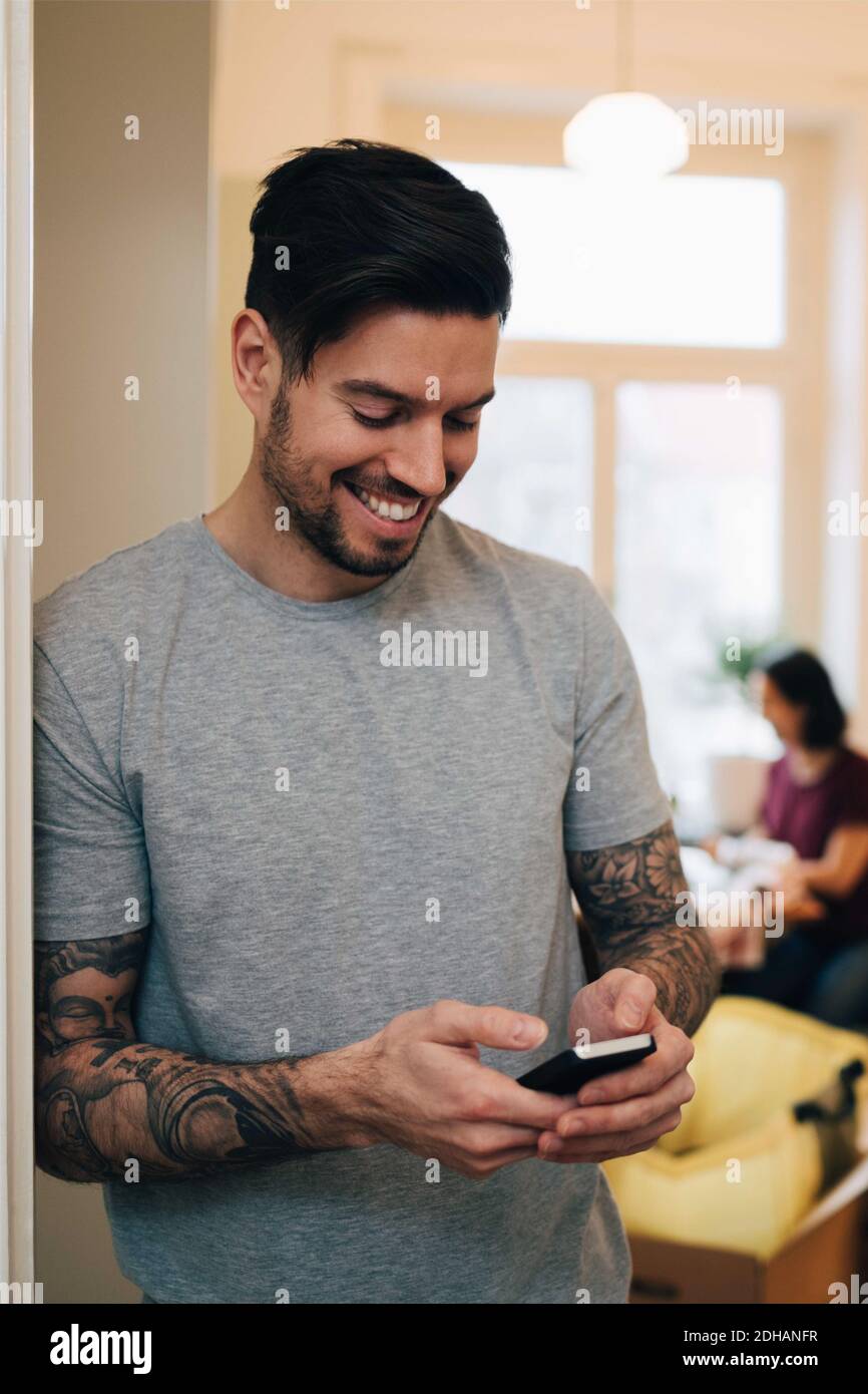 Smiling man using mobile phone while leaning on doorway at new home Stock Photo