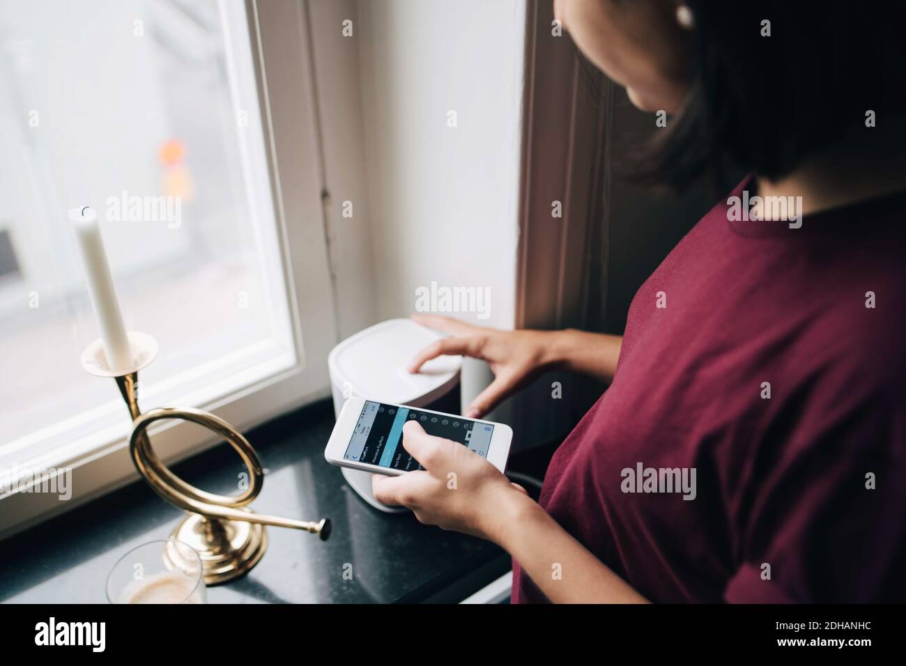 Midsection of woman using smart phone while standing by window Stock Photo