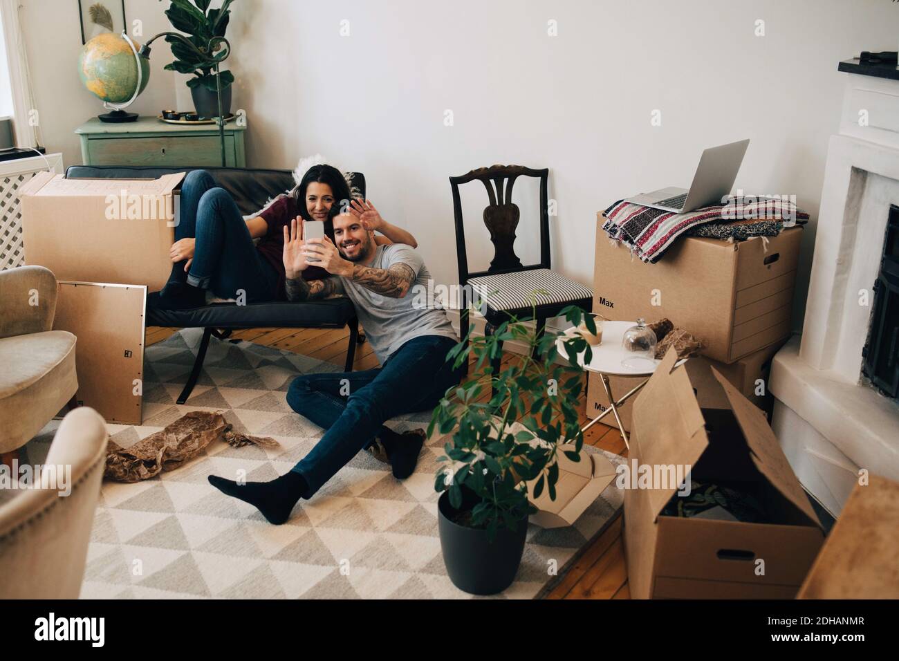Smiling couple video calling through mobile phone while sitting in living room during relocation Stock Photo