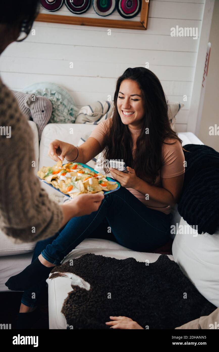 Cropped image of friend serving snacks to smiling woman at home Stock Photo