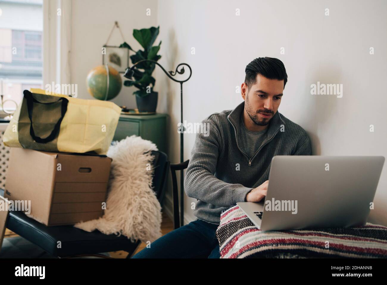 Man using laptop while sitting by boxes at home Stock Photo