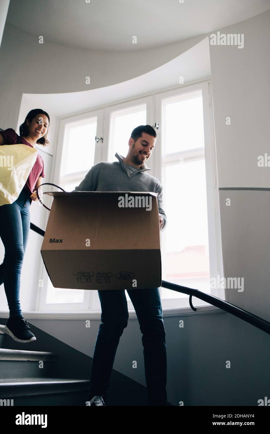 Low angle view of couple carrying box and bag while moving down steps Stock Photo