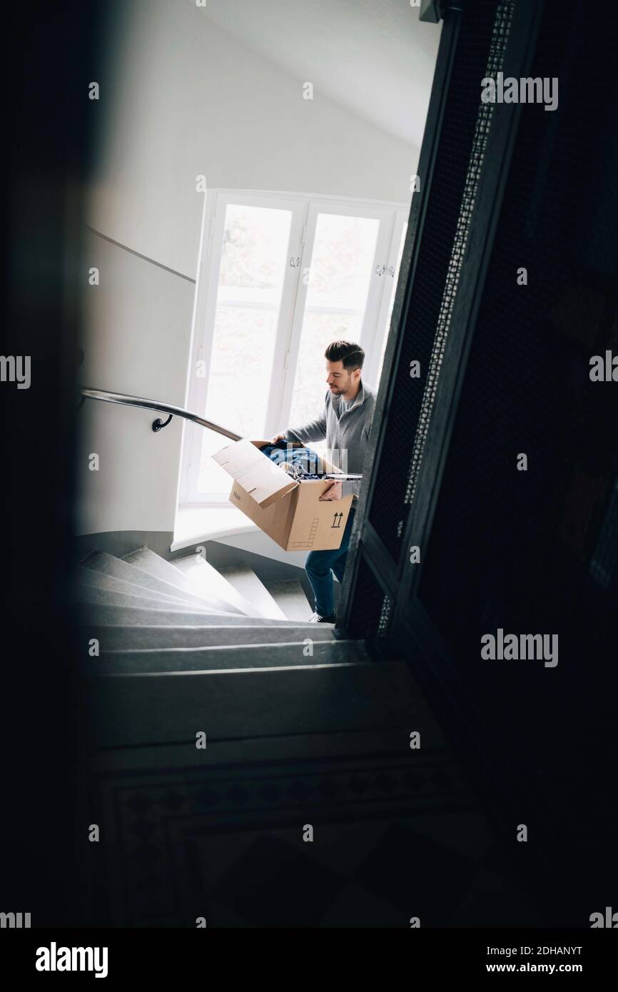 Man carrying box while moving up on steps in new house Stock Photo