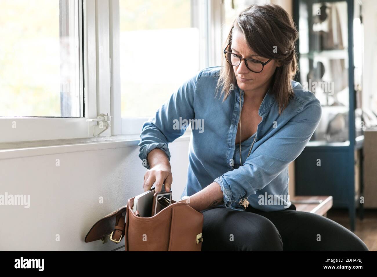 Businesswoman removing laptop from bag while sitting on bench in home office Stock Photo