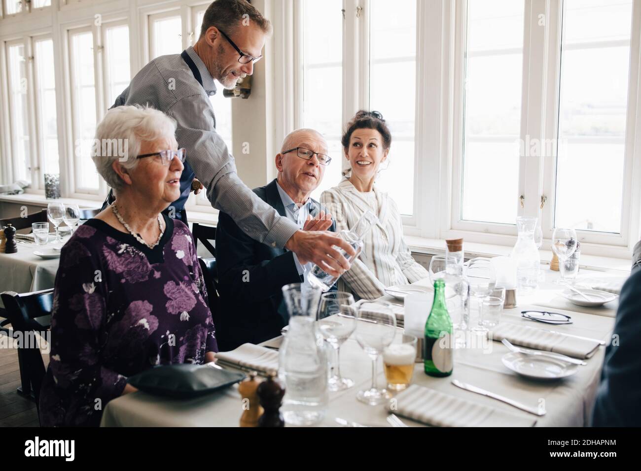 Owner serving water to senior people sitting at restaurant Stock Photo