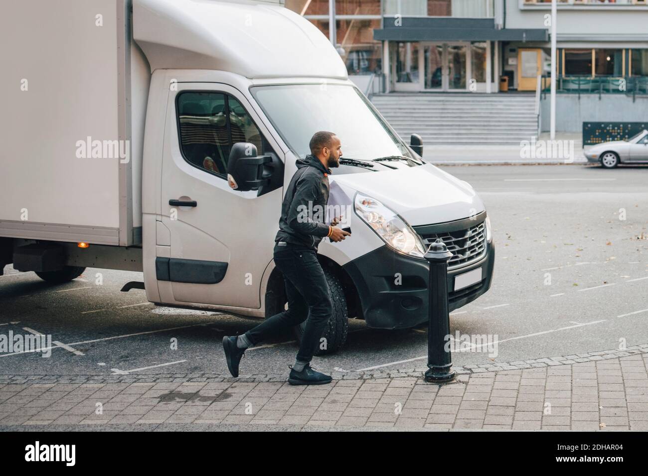 Male messenger with documents running by delivery van on street in city Stock Photo