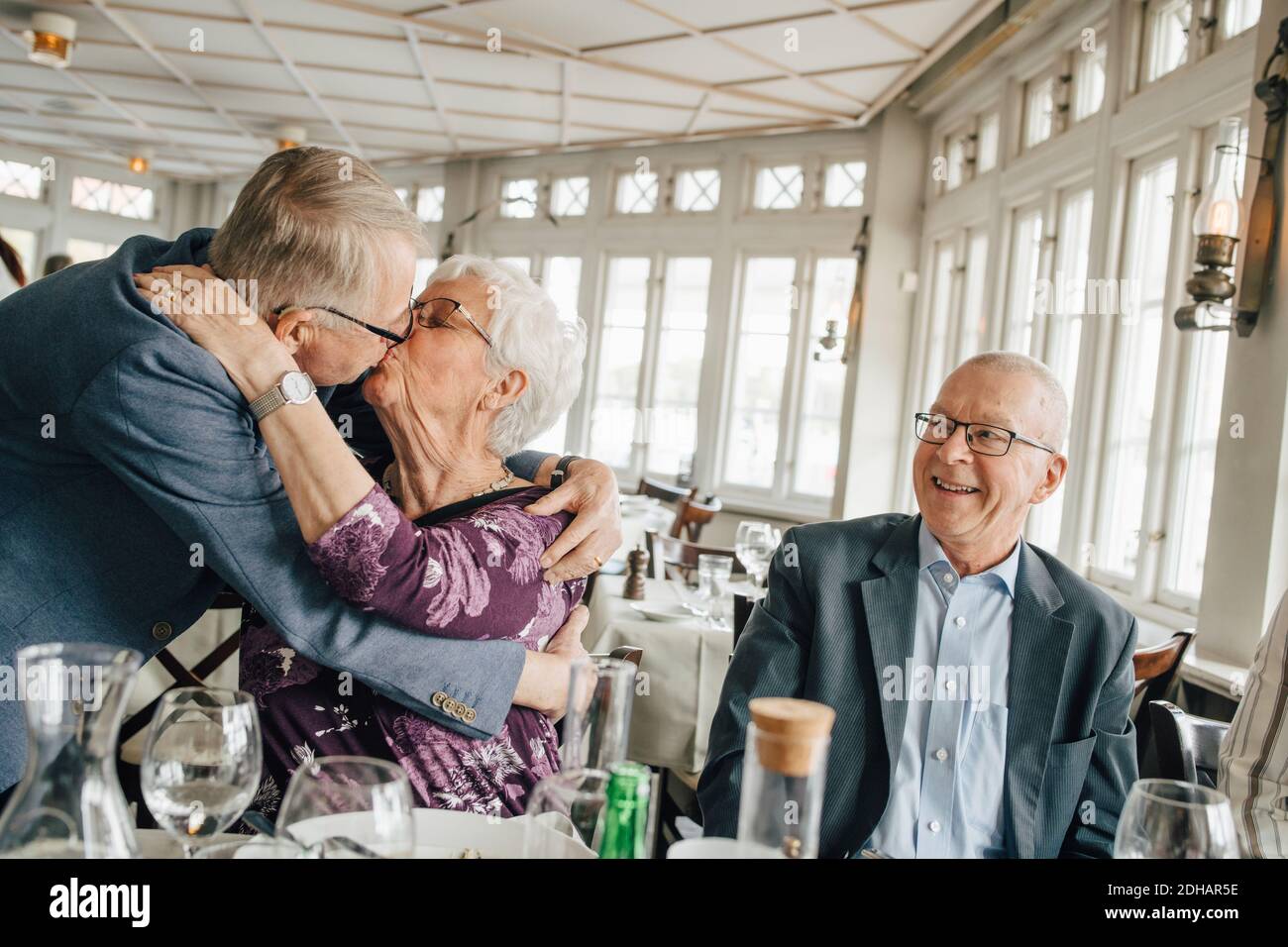 Senior couple kissing while male friend smiling in restaurant Stock Photo