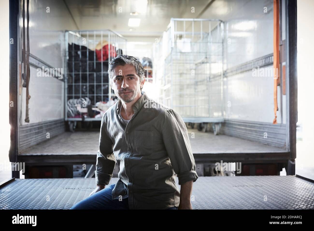 Portrait of mature male volunteer sitting against semi-truck at warehouse Stock Photo