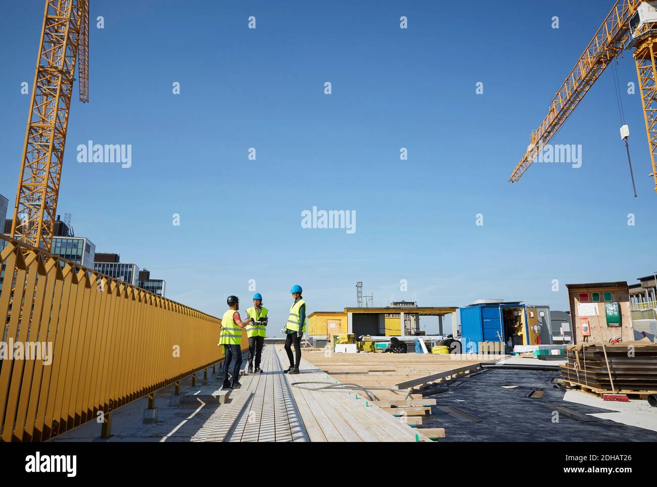 Male and female engineers discussing at construction site against blue sky Stock Photo
