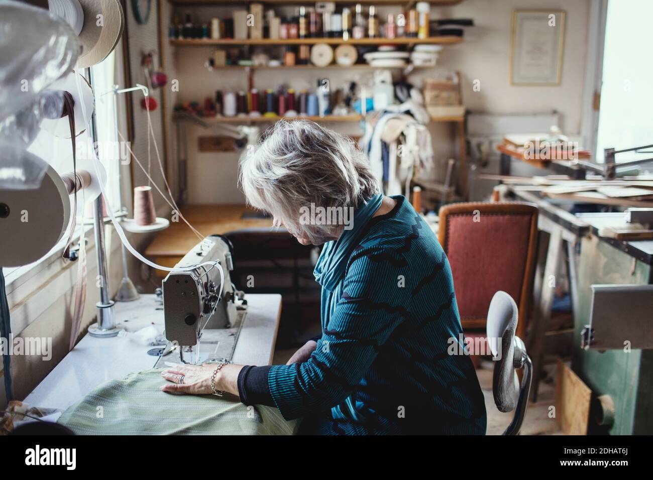 Senior female owner using sewing machine at workshop Stock Photo