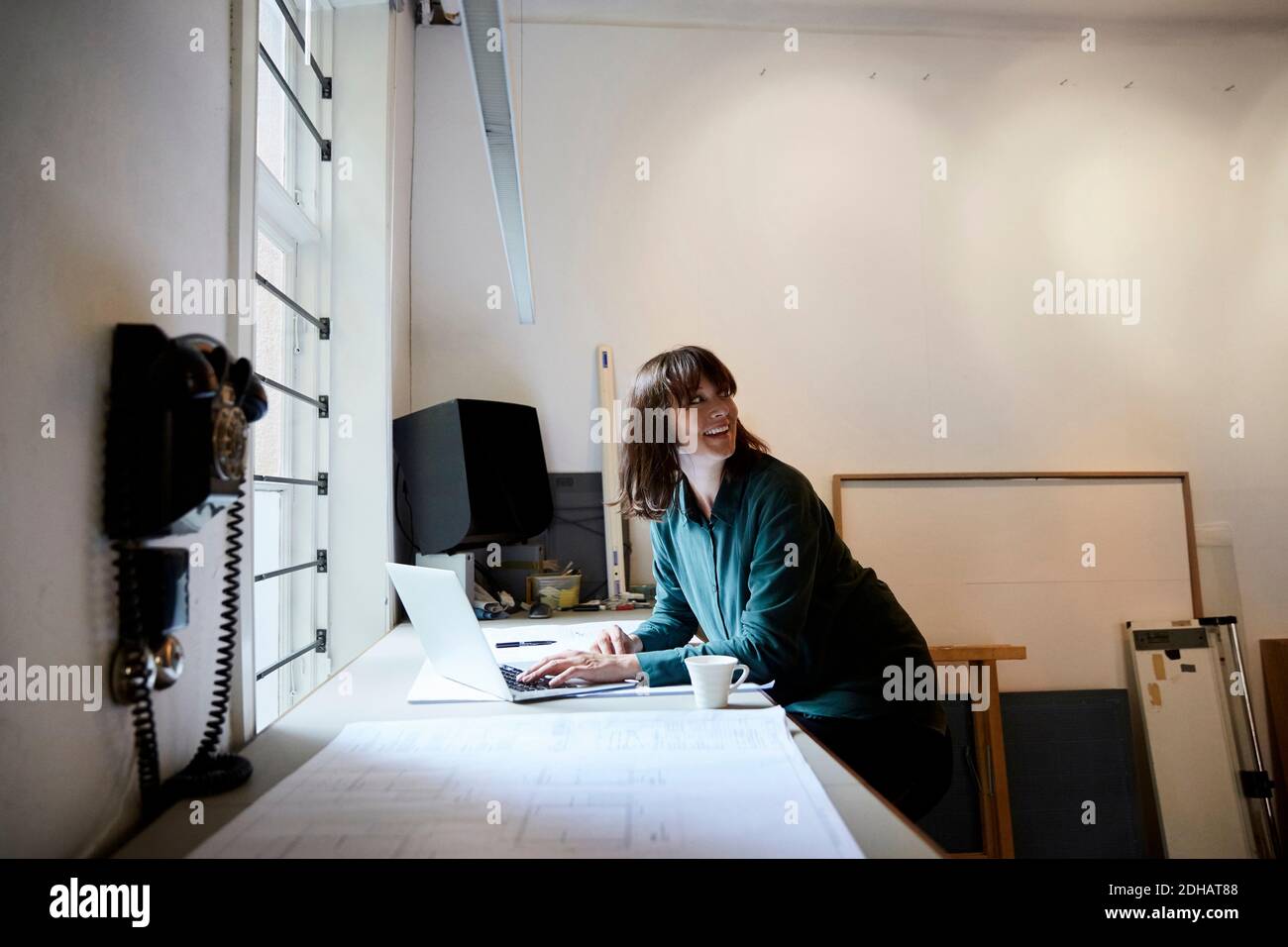 Smiling female architect looking away while using laptop in office Stock Photo