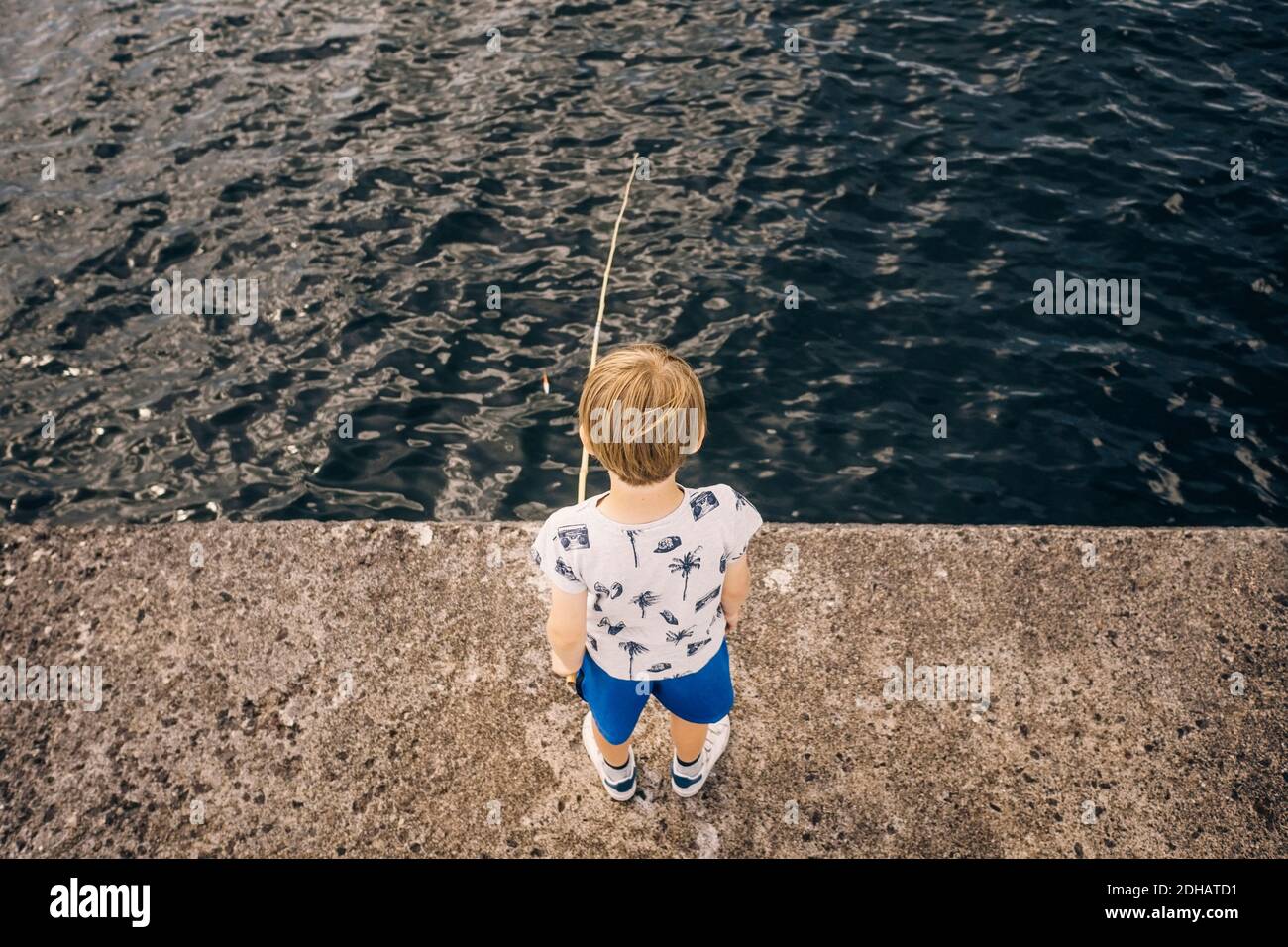 High angle view of boy standing on pier fishing in sea Stock Photo