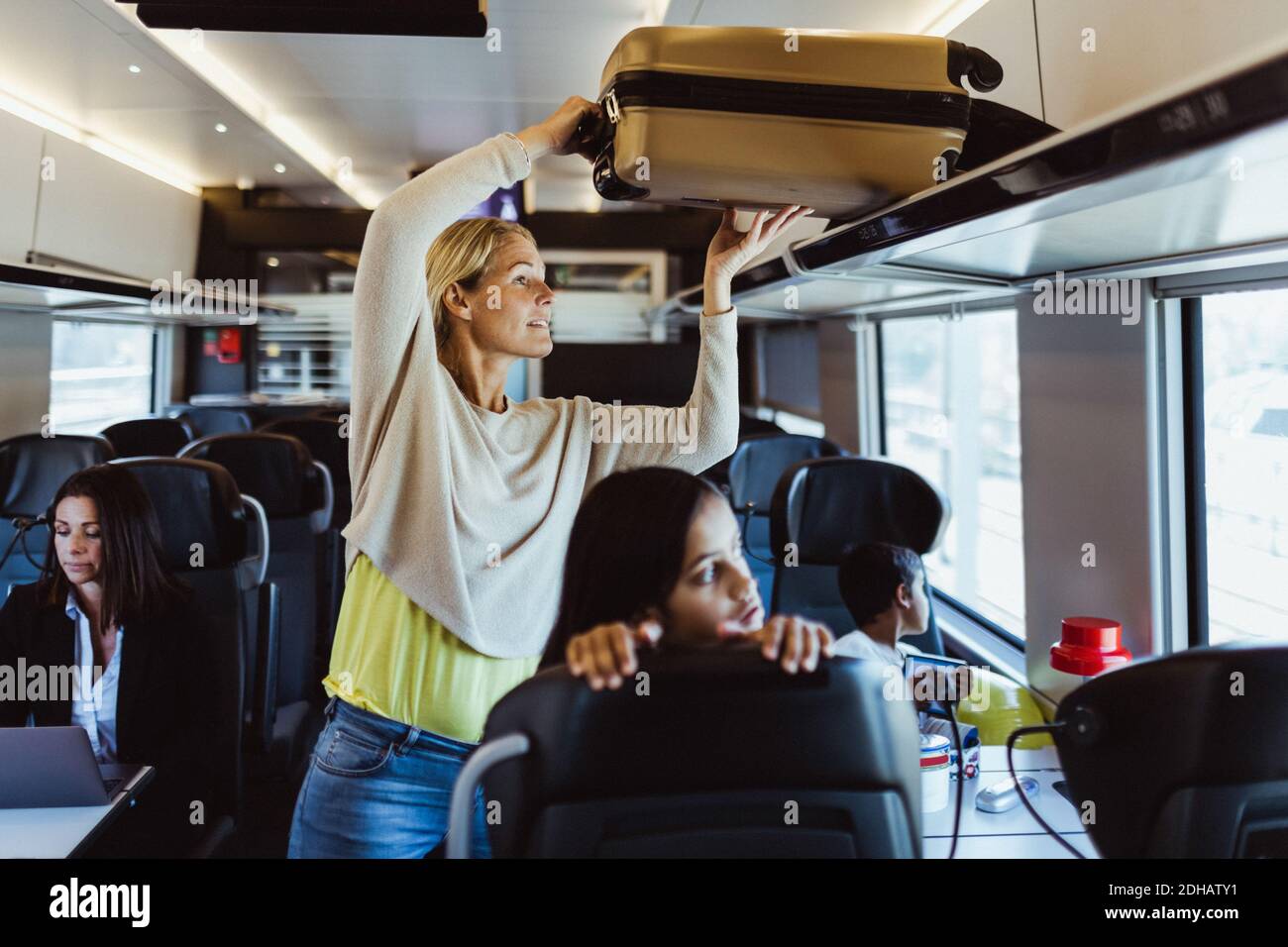 Woman arranging luggage on shelf while traveling with children in train Stock Photo