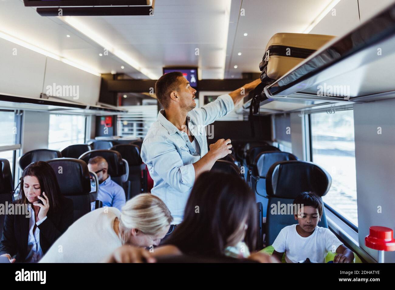 Man adjusting suitcase on shelf while traveling with family in train during vacations Stock Photo