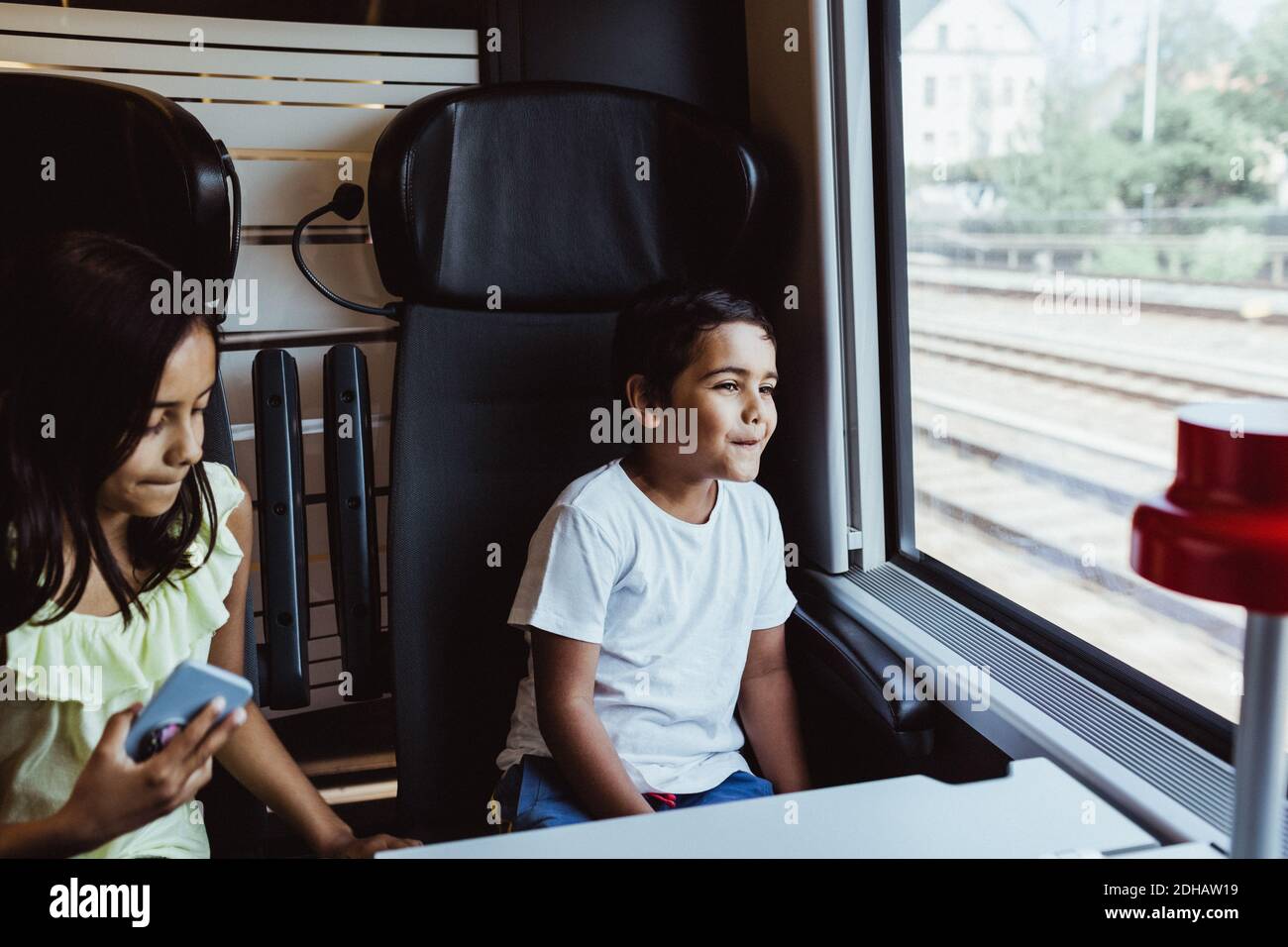 Boy looking through window while sitting with sister in train Stock Photo