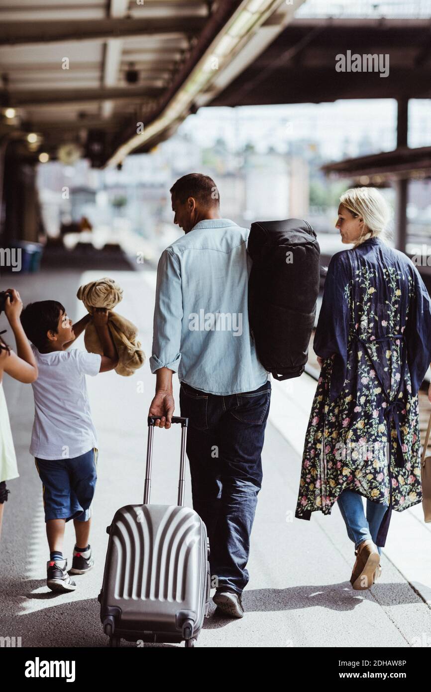 Rear view of man holding luggage while walking with family at railroad station Stock Photo