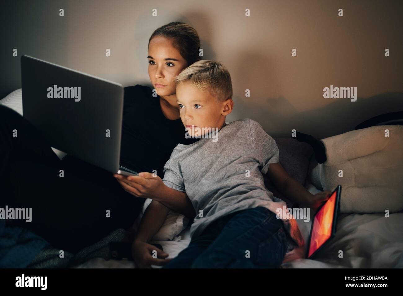 Boy with digital tablet reclining on bed by sister using laptop at home Stock Photo