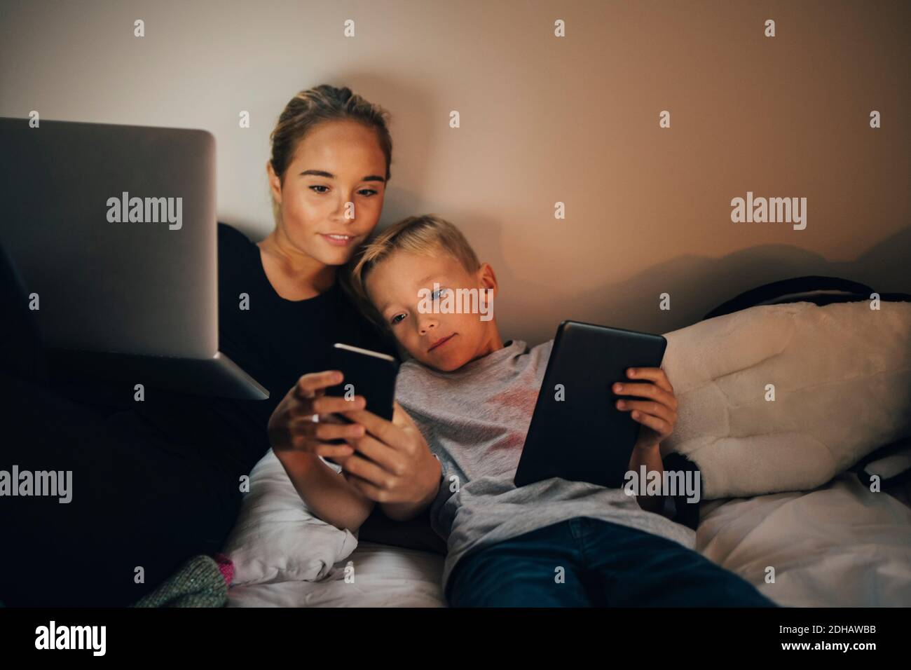 Siblings reclining on bed while sharing smart phone at home Stock Photo