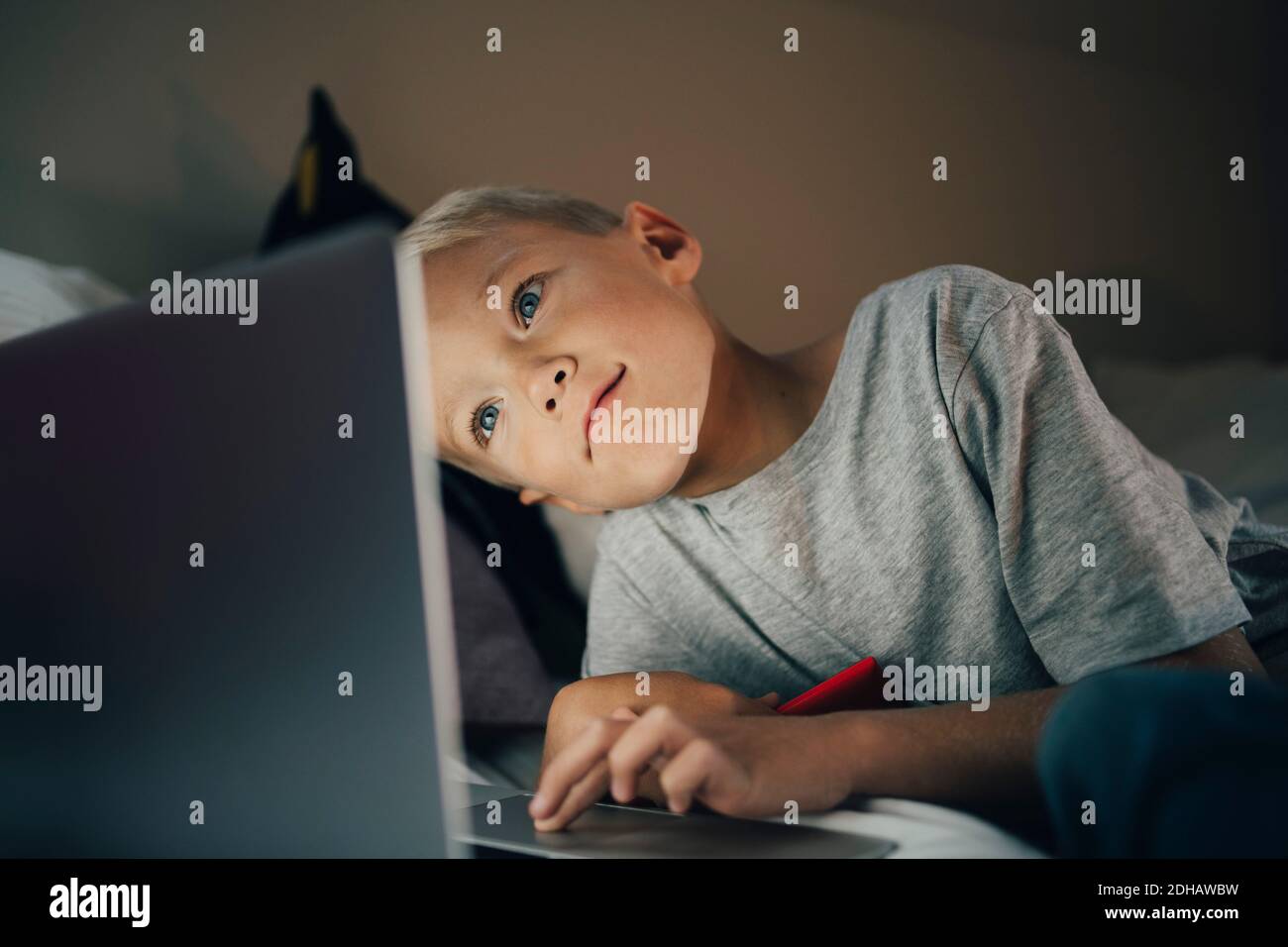 Boy using laptop reclining on bed at home Stock Photo