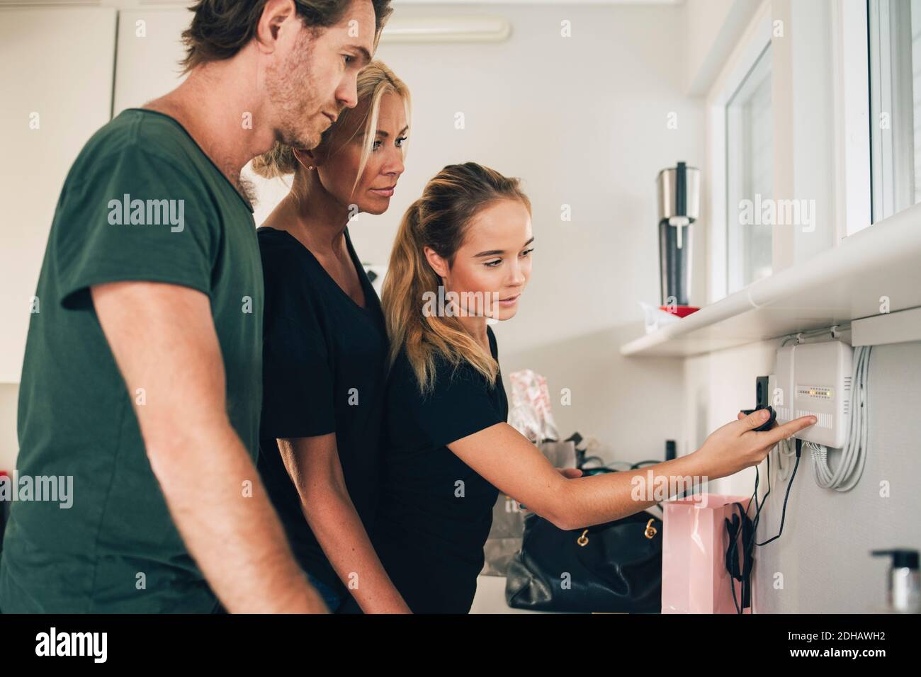 Teenage girl pointing at equipment mounted on wall to parents at home Stock Photo