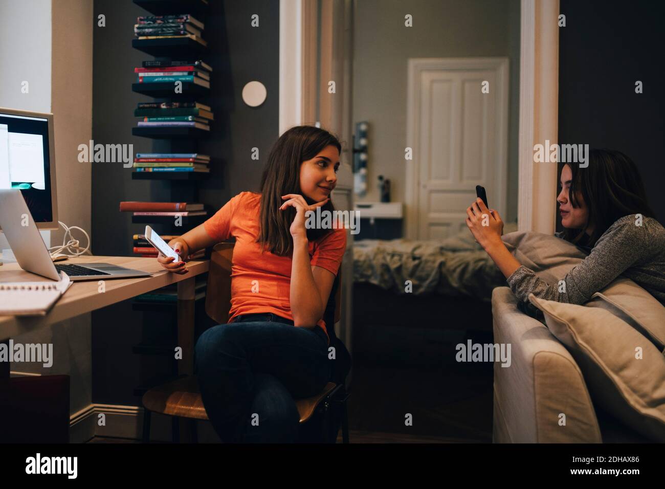 Friends using phone and talking while sitting at home Stock Photo