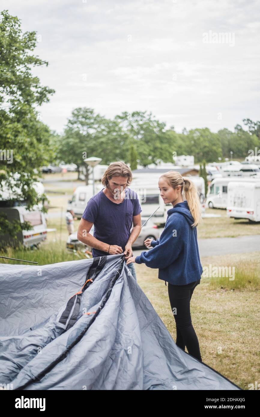 Teenage girl assisting father in pitching tent at campsite Stock Photo