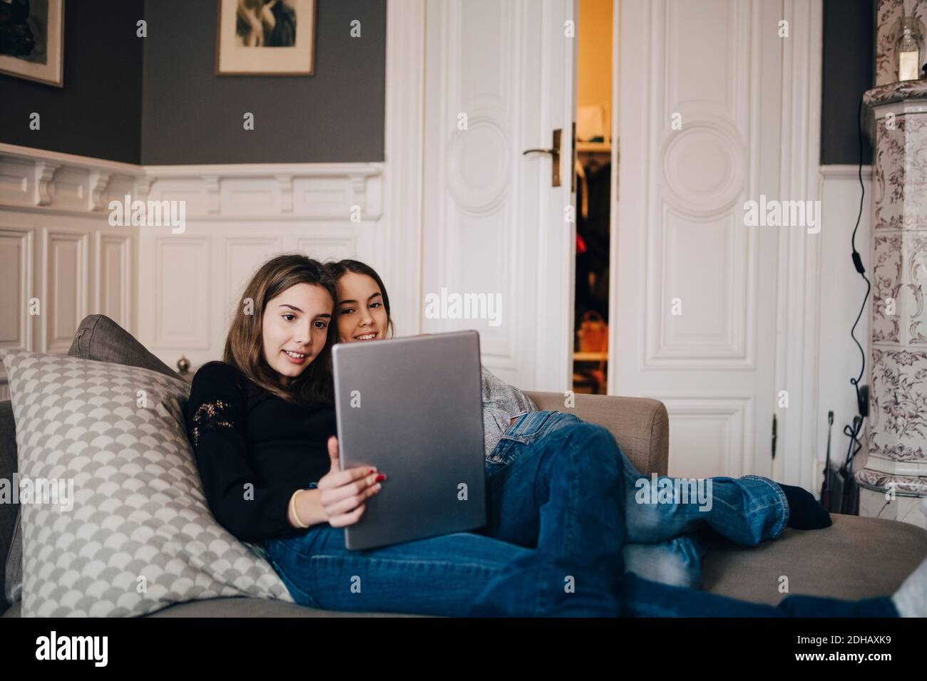 Smiling girls using laptop while resting on sofa at home Stock Photo