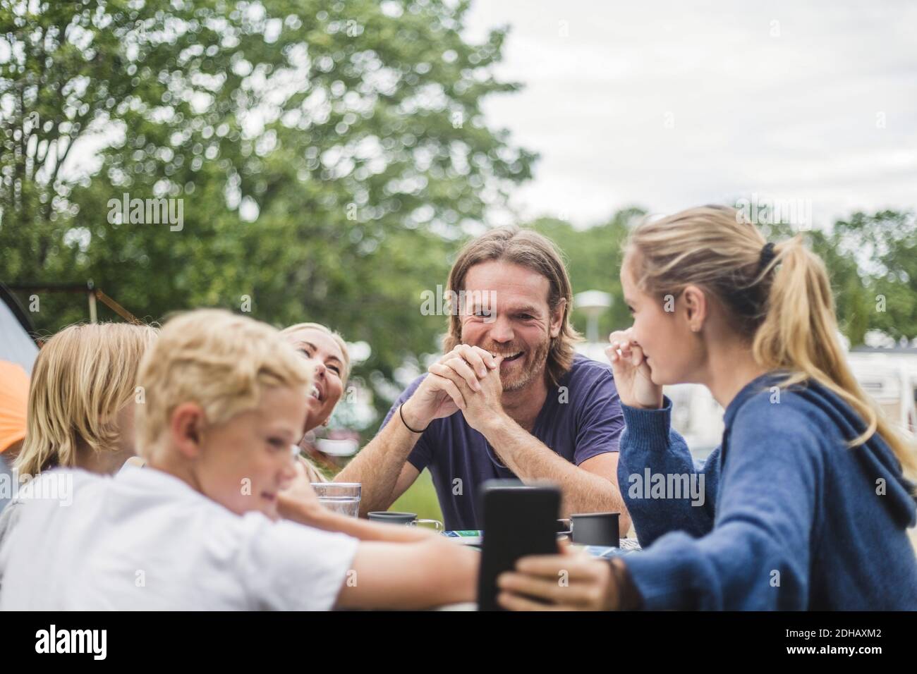 Teenage girl taking selfie with family on table at camping site Stock Photo