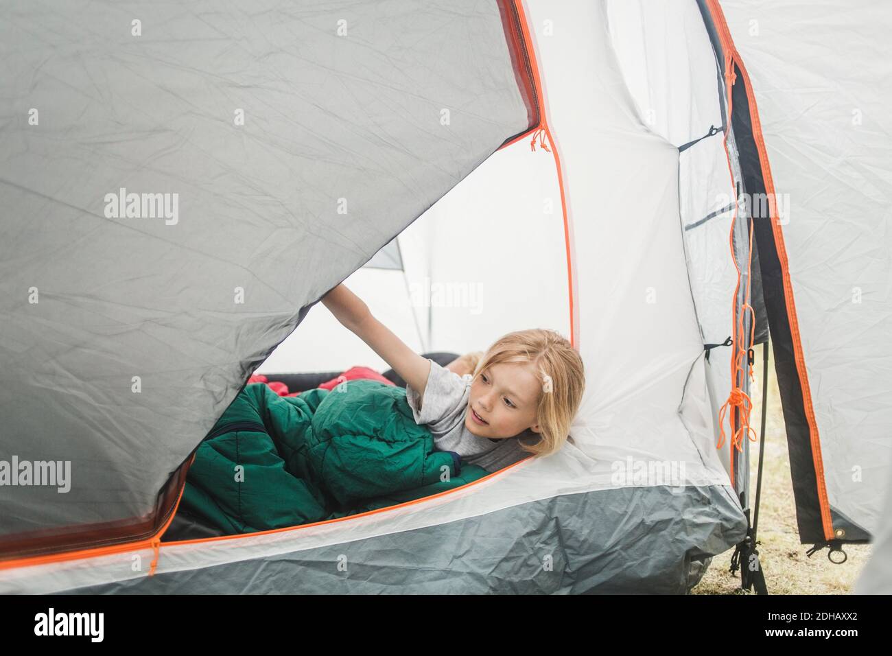 Girl in sleeping bag peeking through tent at camping site Stock Photo