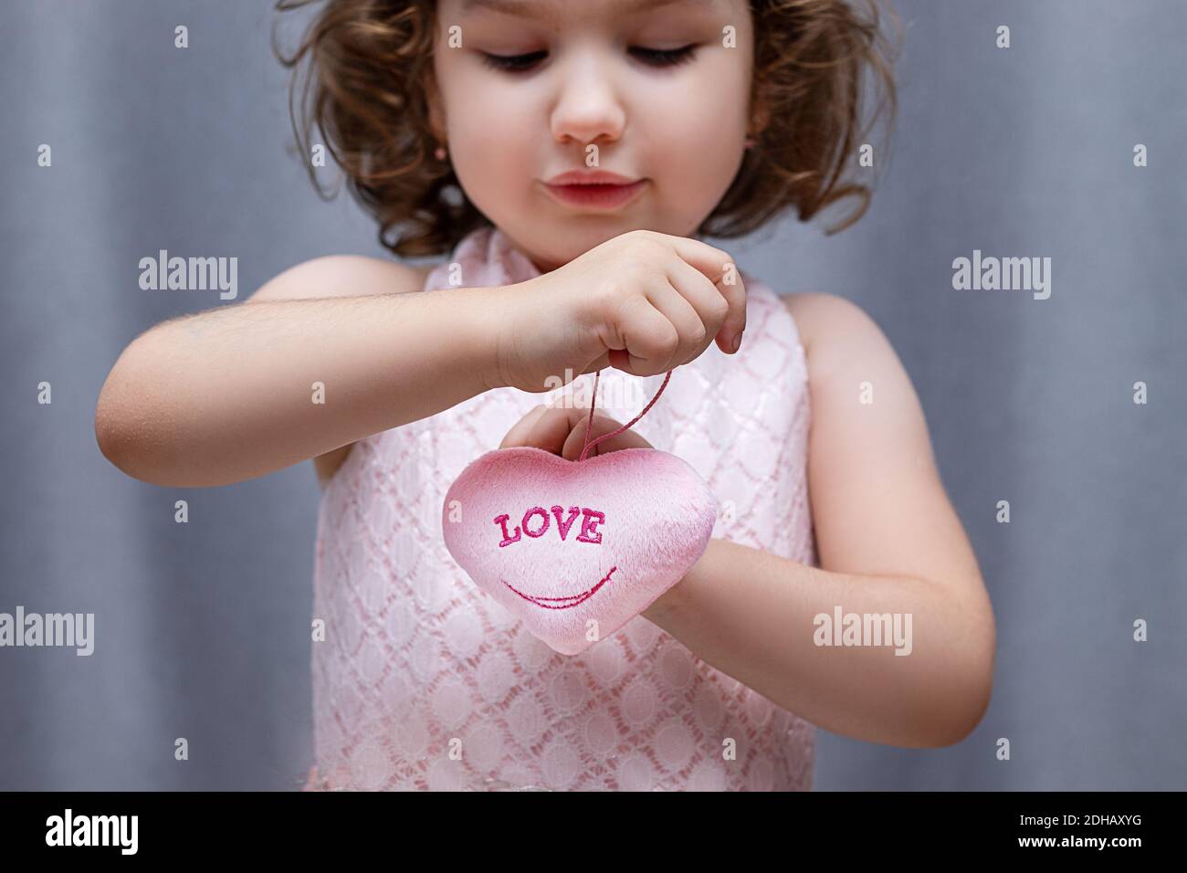 Pink soft toy in the shape of a heart in the hands of a girl 4-5 years old with the inscription Love. Valentine's Day for Valentine's Day. Close-up Stock Photo