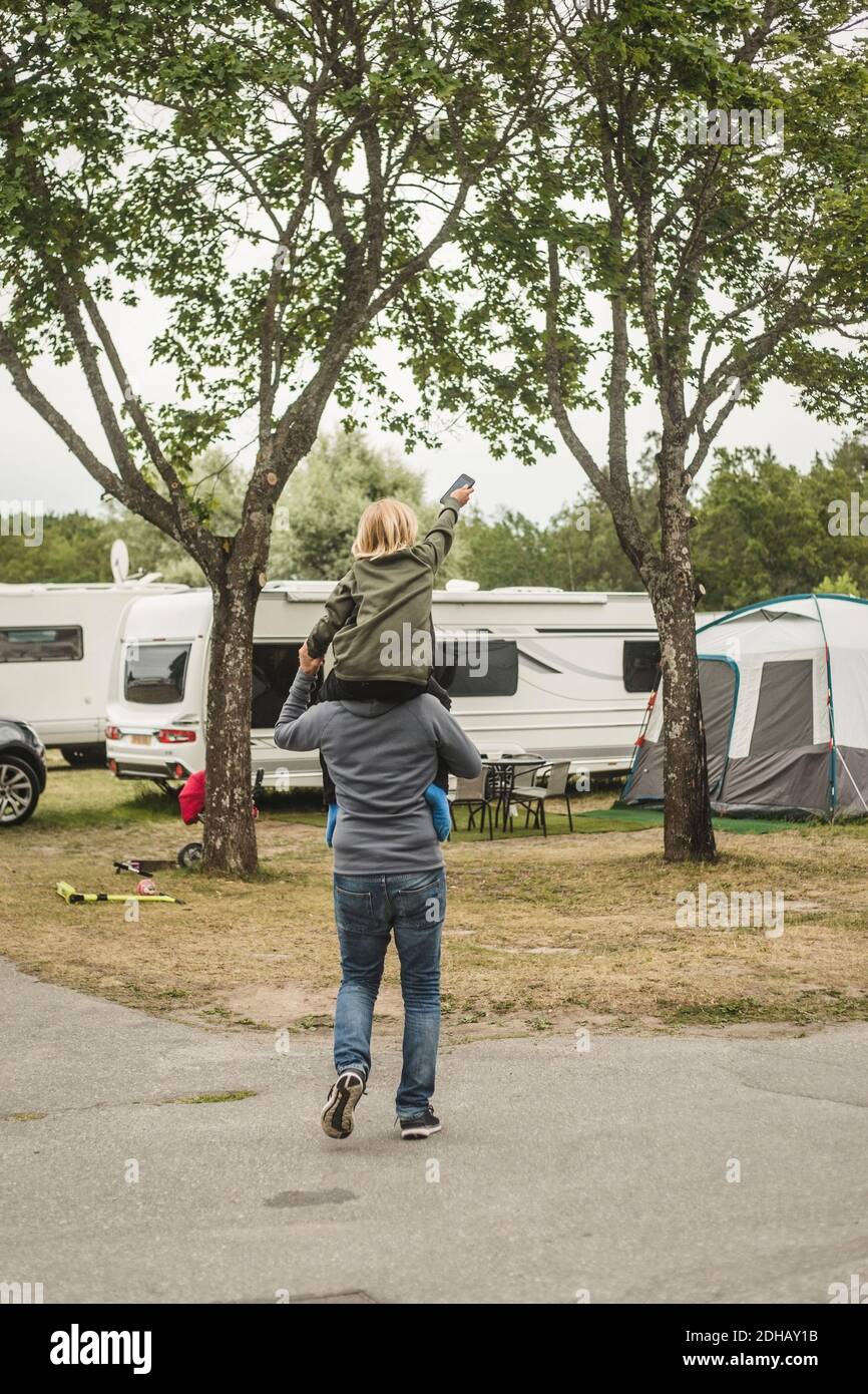 Rear view of father carrying girl on shoulders while standing against camper van Stock Photo