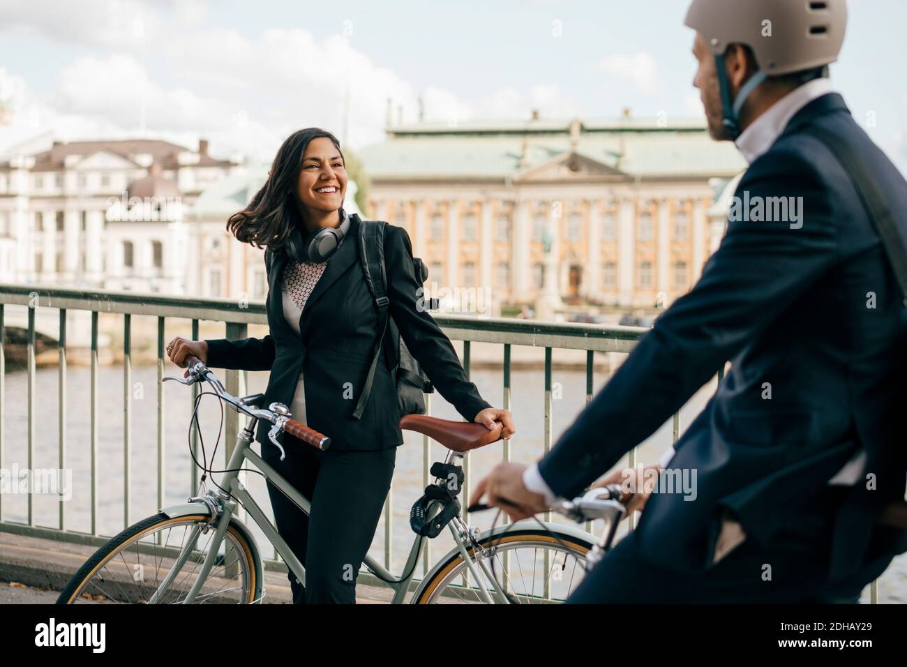 Smiling businesswoman with bicycle looking at colleague biking on bridge Stock Photo