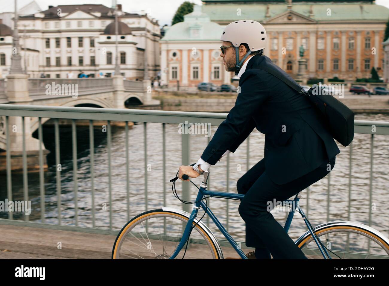 Side view of businessman riding bicycle on bridge by canal in city Stock Photo