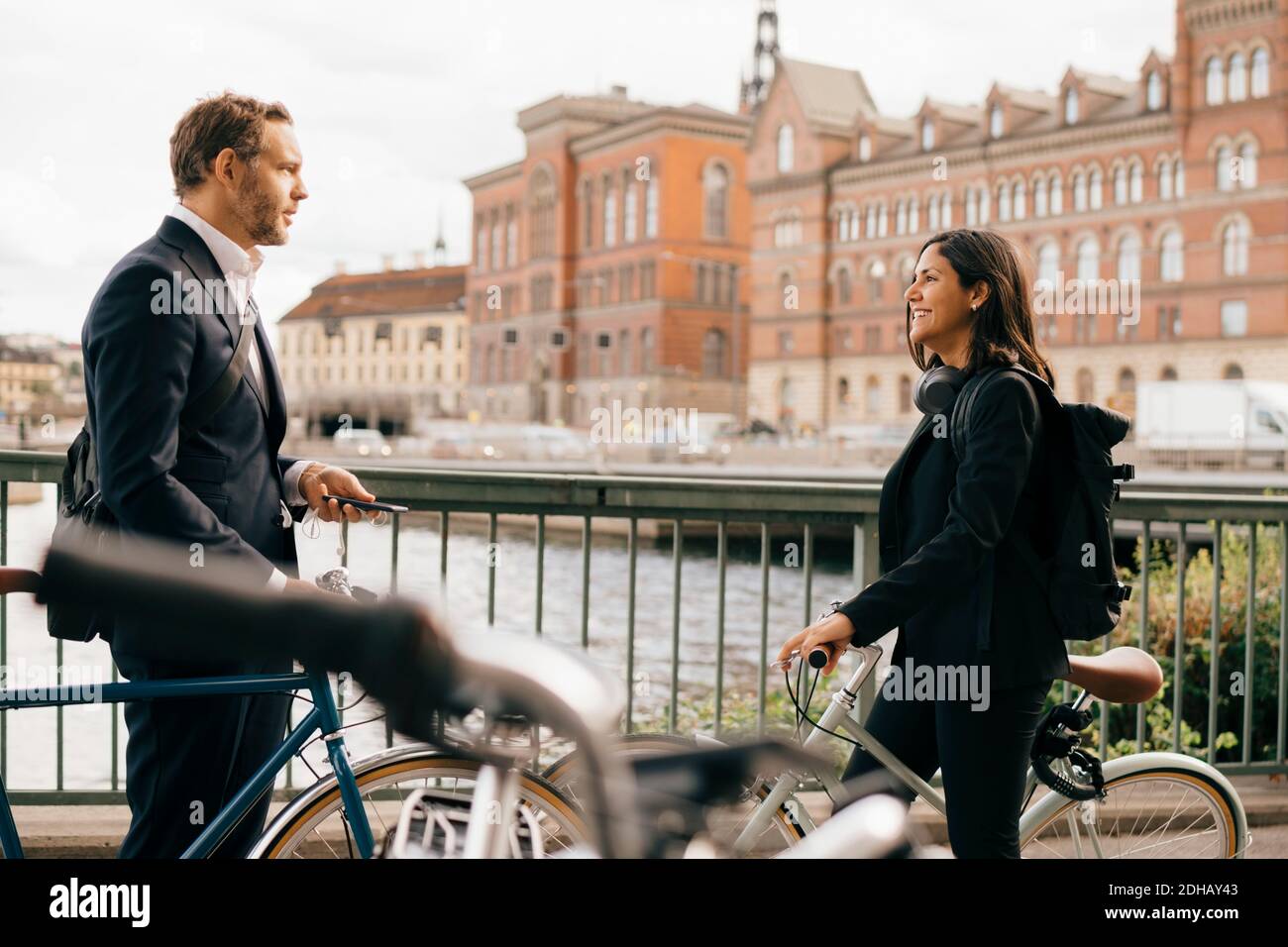 Smiling businesswoman talking with businessman on bridge while biking in city Stock Photo