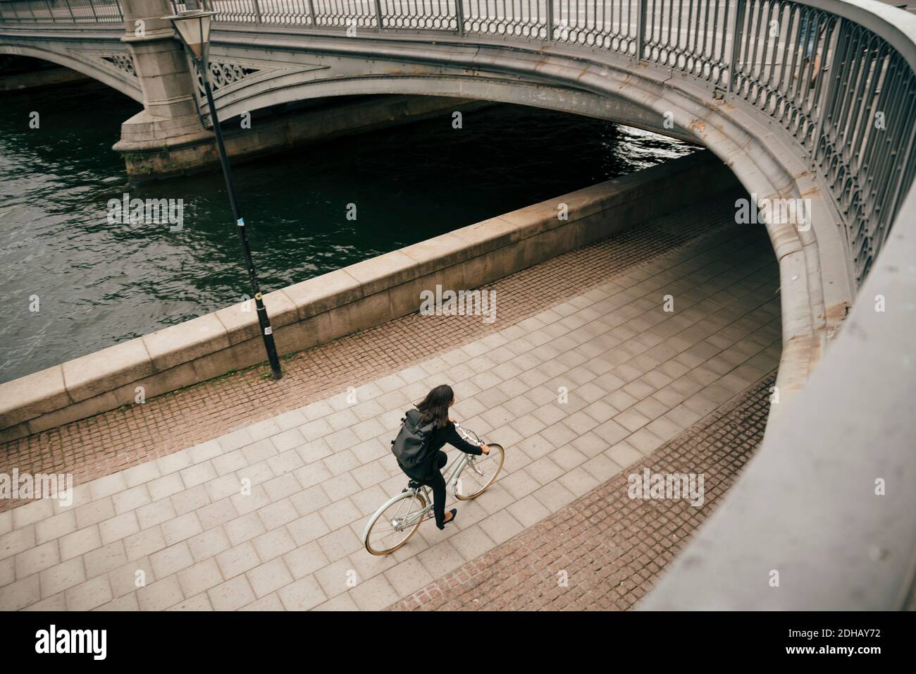 High angle view of businesswoman riding bicycle on footpath by canal in city Stock Photo