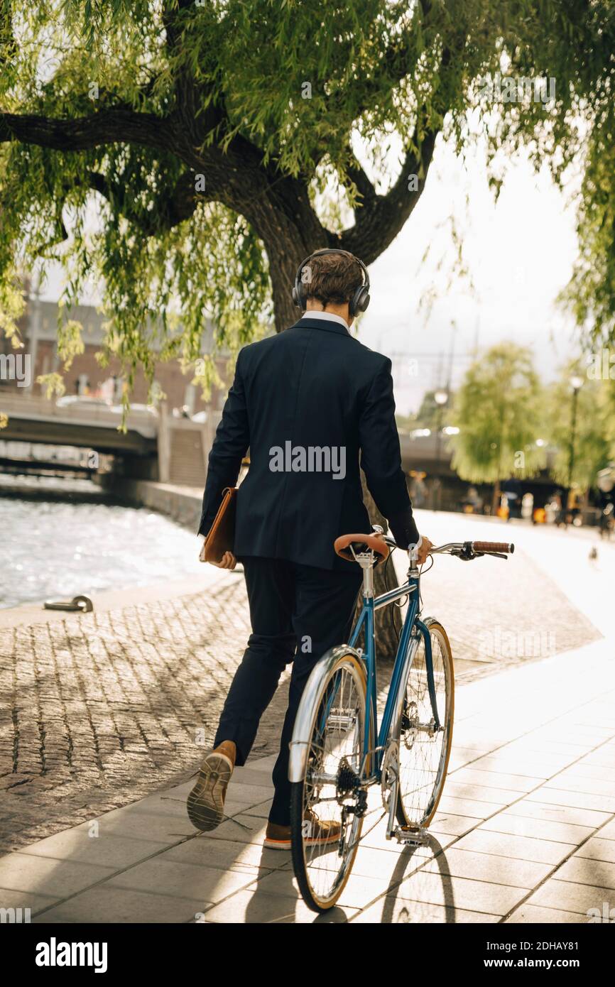Rear view of businessman walking with bicycle on footpath in city Stock Photo