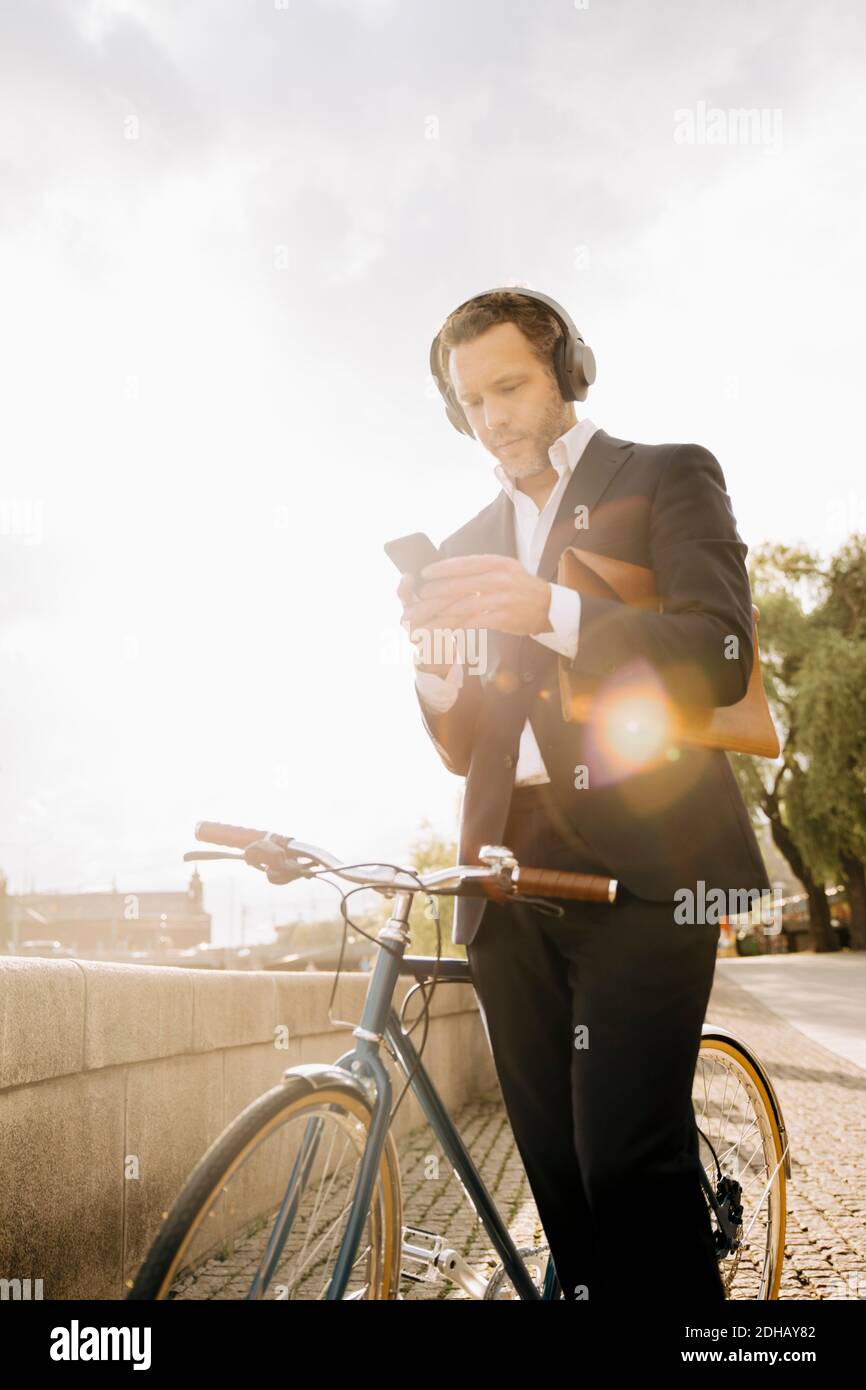 Businessman using mobile phone while standing by bicycle against sky during sunny day Stock Photo