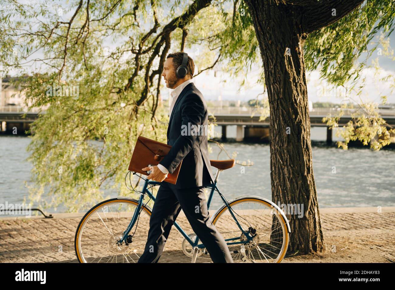 Side view of businessman walking with bicycle on footpath while listening music through headphones Stock Photo