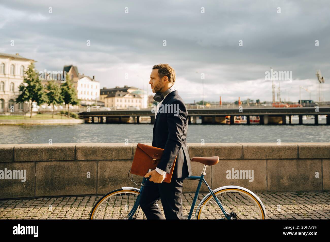 Side view of businessman walking with bicycle on footpath in city against sky Stock Photo