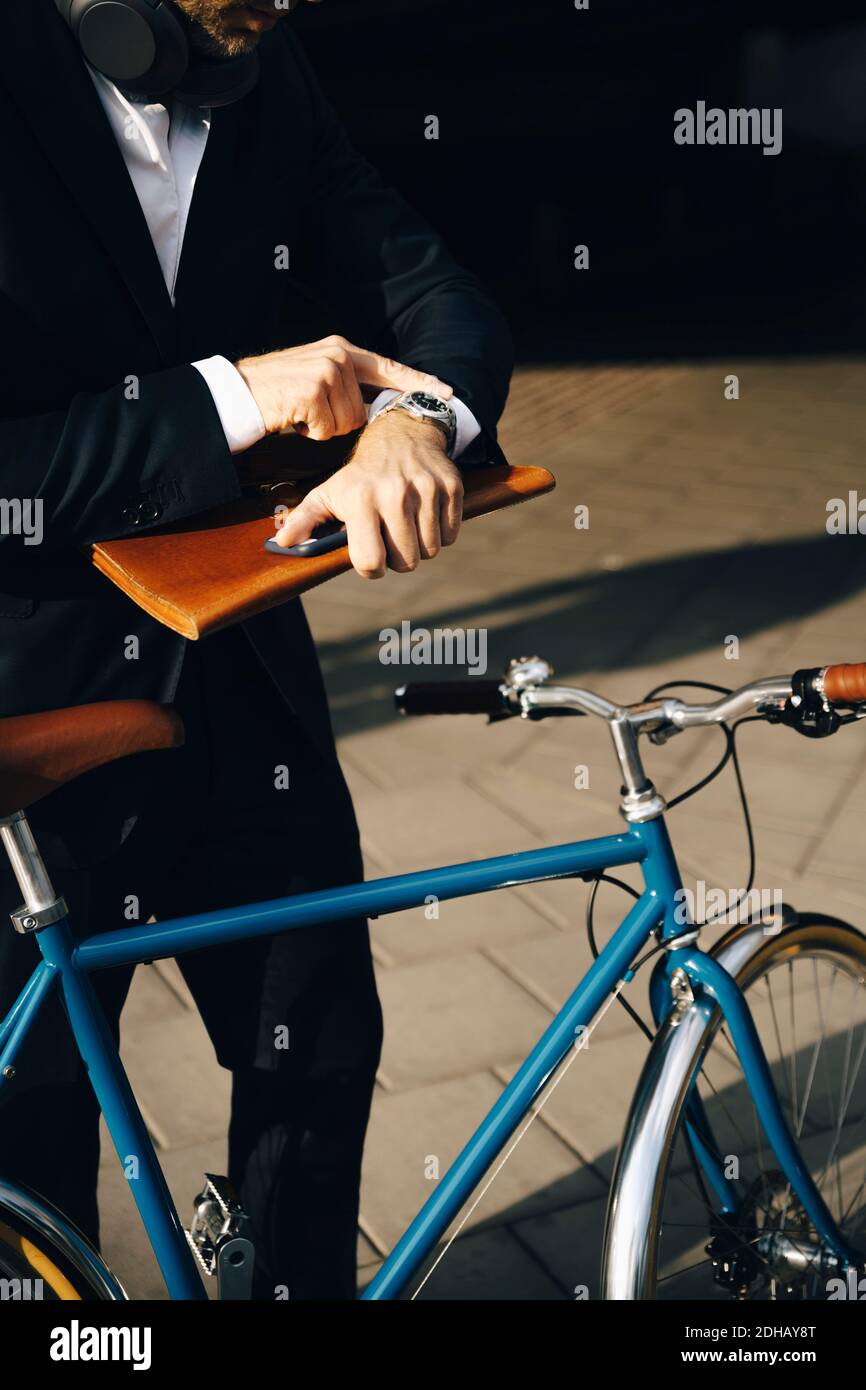 Midsection of businessman checking time while standing by bicycle on footpath in city Stock Photo