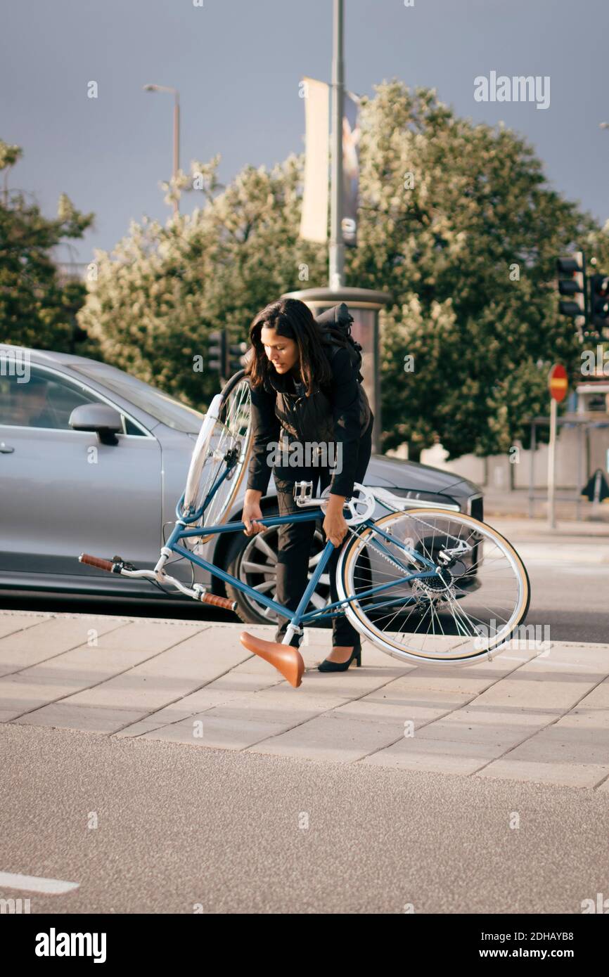 Businesswoman holding bicycle while crossing street in city Stock Photo